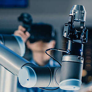 Close-up of a robotic arm being tested by an engineer with virtual reality headset and joystick.